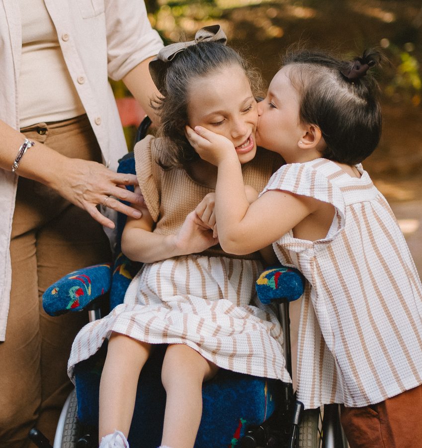 Irmã beijando o rosto da menina no colo da mãe, durante ensaio de família.