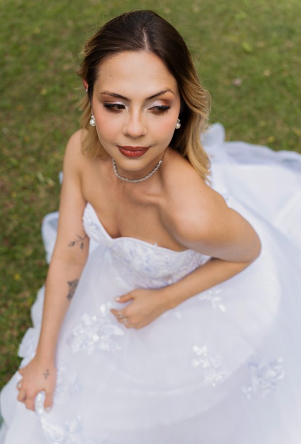 Noiva sentada no gramado com o vestido espalhado ao redor.