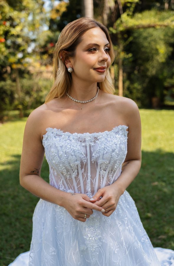 Noiva em pé no jardim, com vestido bordado.