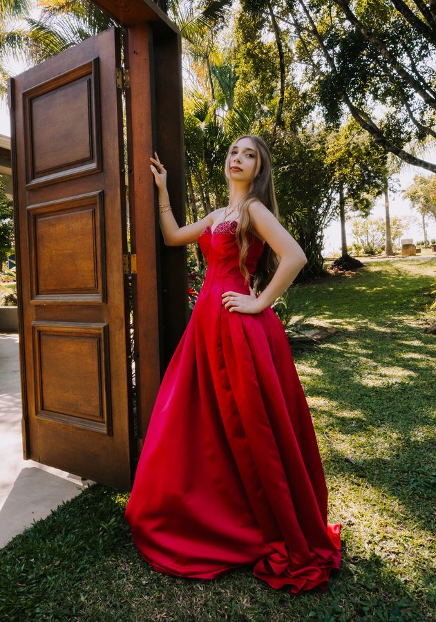 Ensaio com vestido vermelho longo em frente a uma porta de madeira.